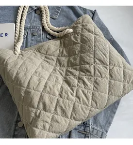 Detail of light khaki quilted nylon tote bag with white rope handles on denim