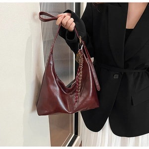 Detail of burgundy hobo bag in oil wax leather with woven texture charm on a model