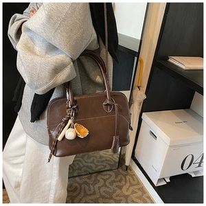 Detail of deep brown PU leather bag featuring creative baseball charms and white stitching