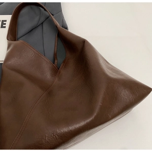 Detailed macro view of deep brown faux leather tote bag with grainy texture and wide strap