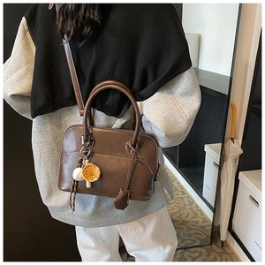 Detail view of dark brown leather crossbody bag with a baseball glove charm accessory