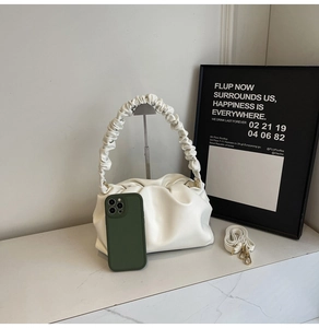Detailed view of white pleated pouch bag with scrunchie handle and removable shoulder strap