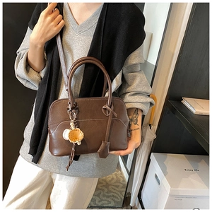 Detail of dark brown faux leather bag with white contrast stitching and baseball charm