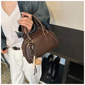 Detail einer dunkelbraunen Boston-Tasche aus PU-Leder mit Baseball-Anhänger und Markenprägung