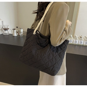 Detail of black quilted tote bag with white rope handles and diamond lattice texture