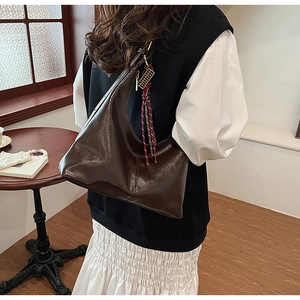 Detail of a dark brown glossy PU leather hobo bag with a woven decorative charm