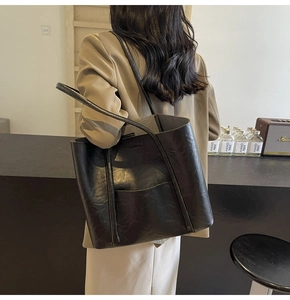 Detail of black faux leather tote bag with textured finish and side pocket shown on model