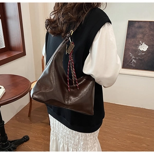 Deep brown glossy leather tote bag with braided fringe detail worn over the shoulder