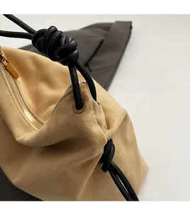 Détail du sac bandoulière en daim avec œillets dorés et poignée en corde tressée noire