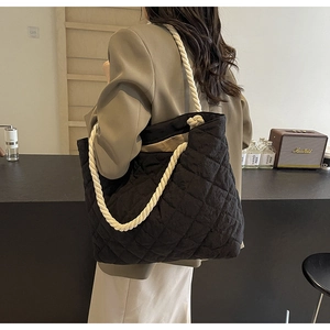 Detail view of large quilted black tote bag with white woven rope shoulder straps