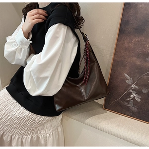Detail of a dark brown PU leather hobo bag with a red and white woven rope charm