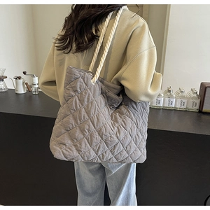 Detail view of quilted grey tote bag with rope handles worn by model in cafe setting