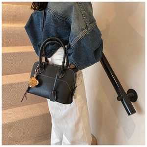 Detail of black PU leather boston bag with white contrast stitching and a small bear charm