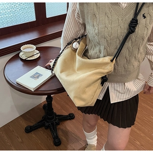Détail du sac hobo en daim avec bandoulière en corde noire nouée et breloque de baseball