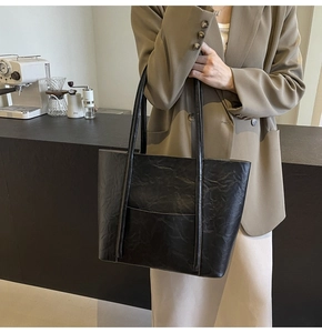 Detail of a large black tote bag with unique pleated texture and a front pocket