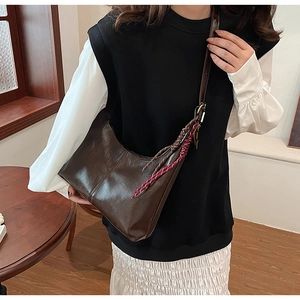 Close-up of dark brown glossy leather crescent bag with braided rope tassel detail