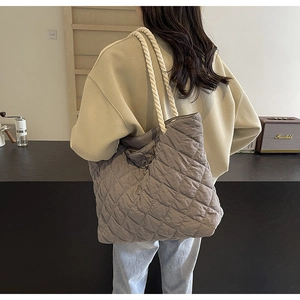 Detail of grey quilted tote bag with white rope strap shown in a lifestyle cafe setting