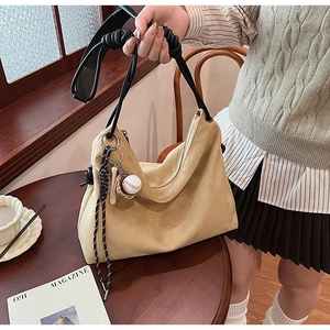 Détail du sac hobo en daim beige avec bandoulière tissée et pendentif de baseball