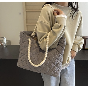 Detail view of gray quilted fabric tote bag with white rope handles on a casual model