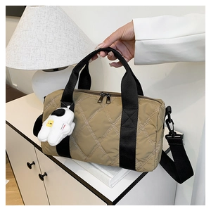 Detail of khaki quilted nylon shoulder bag with astronaut charm in a home setting