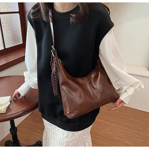 Detail of dark brown leather crescent shoulder bag with woven tassel charm and strap