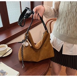 Sac à épaule en daim marron avec poignée nouée et breloque baseball sur une table en bois
