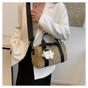 Detail of khaki quilted nylon crossbody bag featuring astronaut plush charm on wide strap