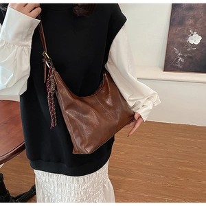 Close-up of caramel brown PU leather crossbody bag with woven tassel and retro minimalist style