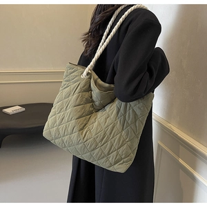 Side view of a sage green quilted tote bag with white woven rope handles on a model