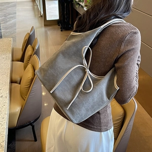 Sac hobo en daim gris avec nœud blanc et liseré contrasté porté par un mannequin