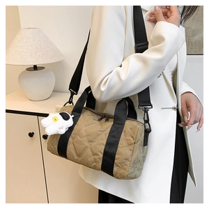 Detail of khaki quilted nylon cylinder bag featuring a black strap and astronaut charm