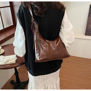 Detail of a dark brown hobo shoulder bag showing glossy PU leather and woven zipper pulls