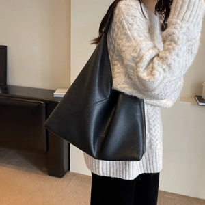 Minimalist black pebbled leather tote bag for women worn over a white cable knit sweater