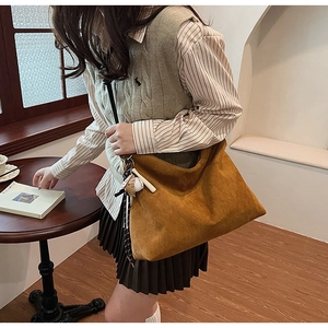Détail du sac Hobo en daim marron avec pendentif de baseball et tons terreux doux