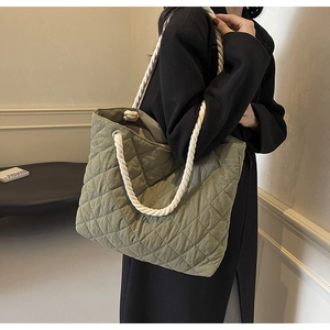Detail view of army green quilted tote bag with thick white rope handle worn by a model