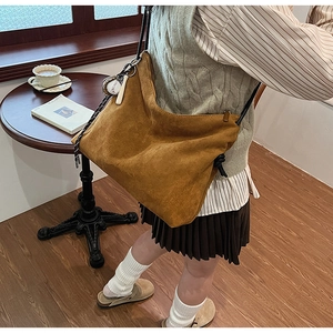 Détail du sac à bandoulière en daim caramel avec breloque de baseball et fines lanières