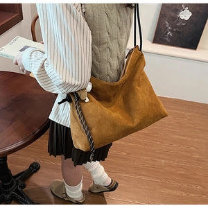 Détail du sac hobo en daim marron caramel avec nœud tressé et bandoulière noire élégante
