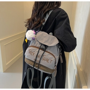 Détail d'un sac à dos en nylon gris avec broderie et un pendentif peluche blanc
