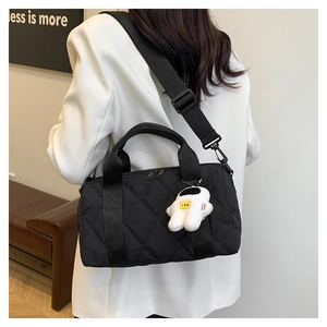 Detail of black quilted nylon bag with wide strap and cute white astronaut plush pendant