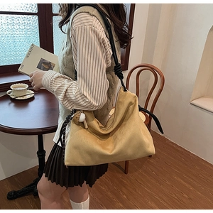 Gros plan d'un sac hobo en daim jaune moutarde avec bandoulière épaisse à nœuds noirs