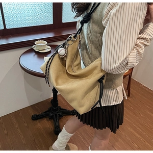 Détail du sac bandoulière en daim kaki avec cordons noirs et pendentif de baseball