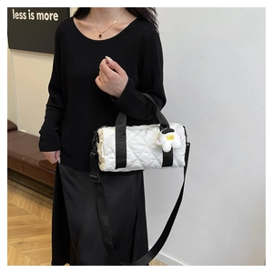 Close-up of white quilted nylon barrel bag with astronaut plush charm and black straps