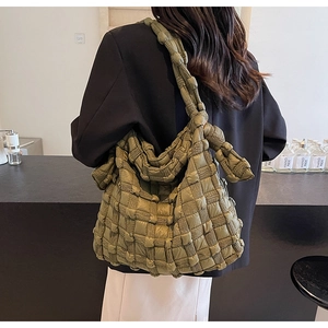 Gros plan du sac à bandoulière tressé vert olive porté par un mannequin en décor épuré