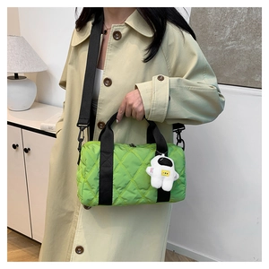 Detail of green quilted nylon handbag with astronaut plush charm on stylish trench coat