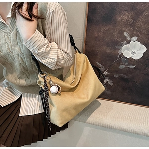 Détail du sac hobo en daim jaune avec bandoulière en corde nouée et breloque baseball