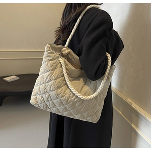 Minimalist beige quilted tote bag shown on model's shoulder in a clean lifestyle setting
