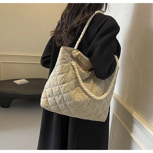 Detail view of beige quilted tote bag featuring a unique thick white rope braided strap