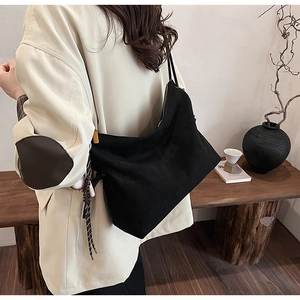 Détail d'un sac à bandoulière minimaliste en daim noir porté par un mannequin