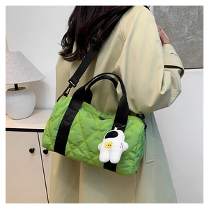 Detail of green quilted nylon cylindrical bag with black straps and astronaut charm