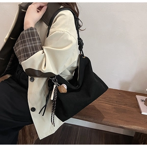 Détail du sac bandoulière en daim noir avec breloques de sport sur banc en bois